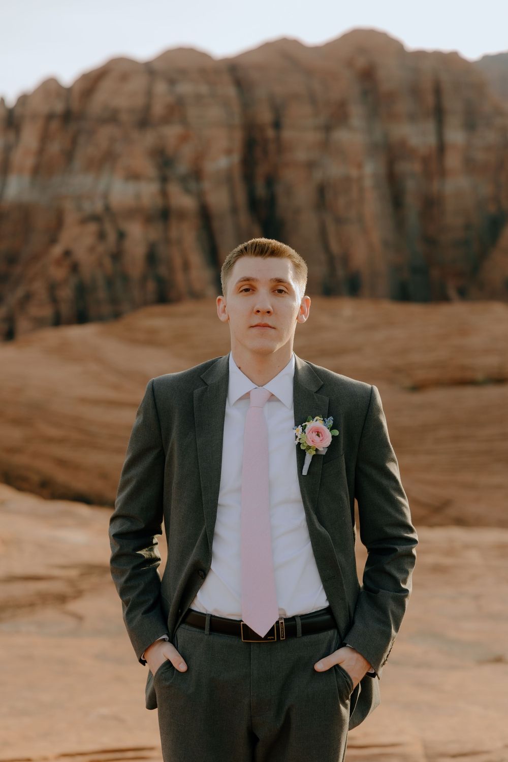 Portrait of a groom wearing grey suit and pink tie against desert canyon backdrop.
