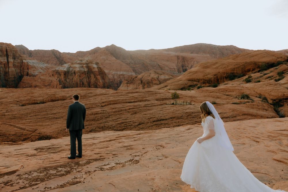 Wedding couple stands apart in dramatic desert landscape during sunset.