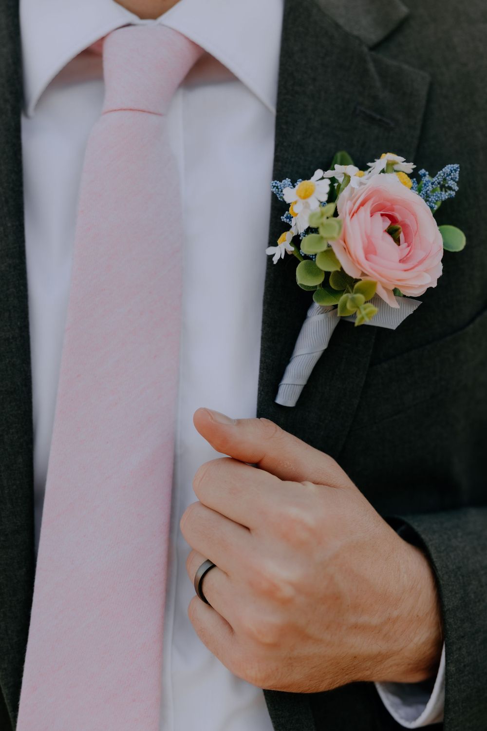 Close up of pink tie, white shirt and floral boutonniere with wedding ring.