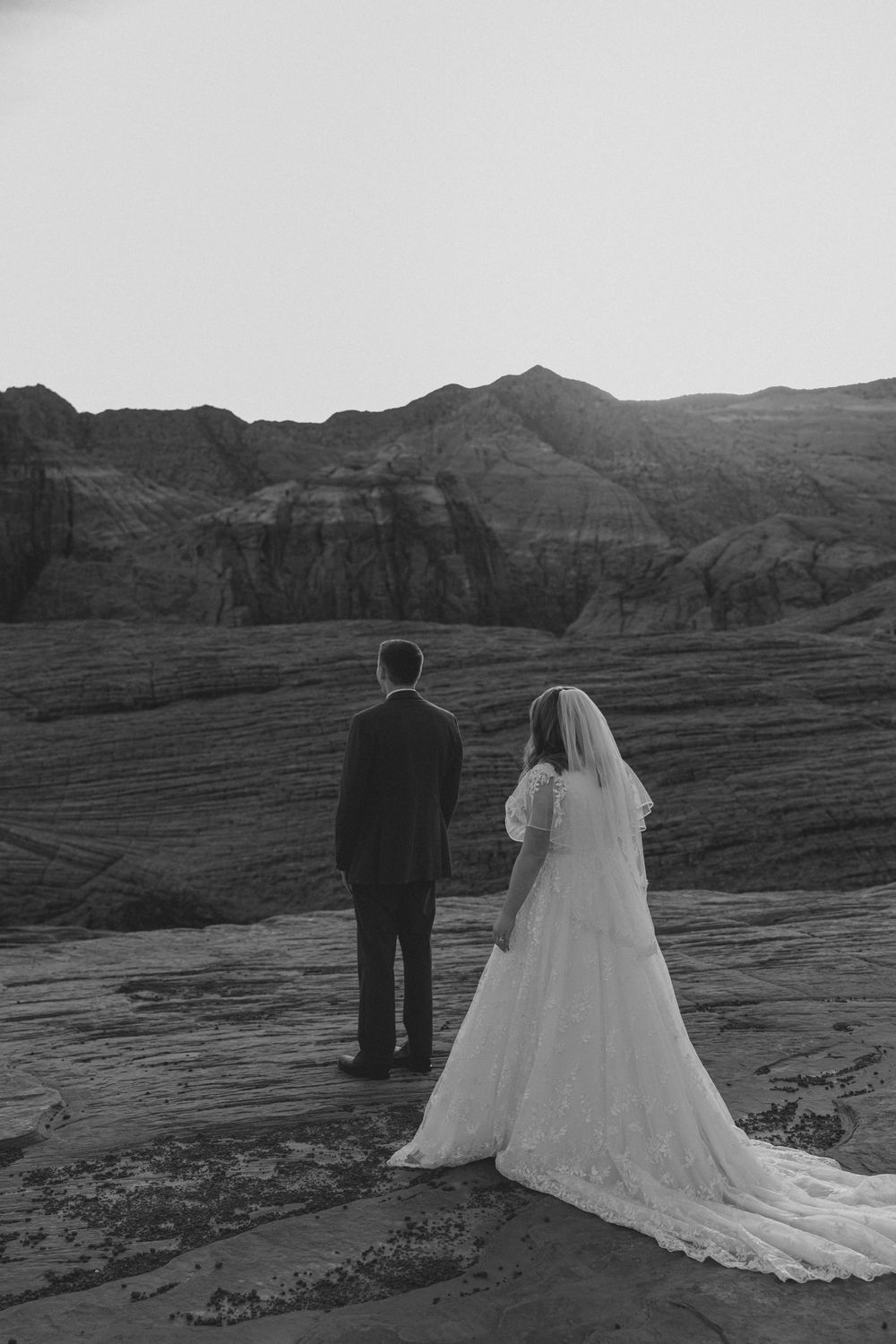 Black and white wedding portrait overlooking dramatic canyon landscape.