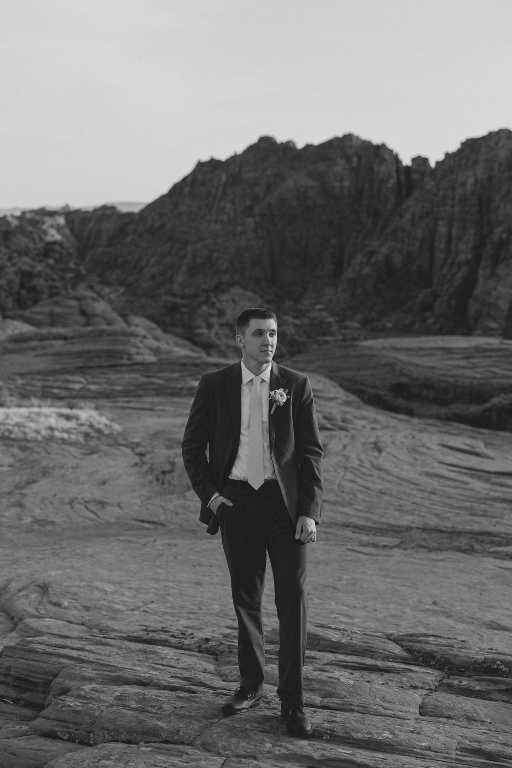 A black and white portrait with towering desert cliffs as backdrop.