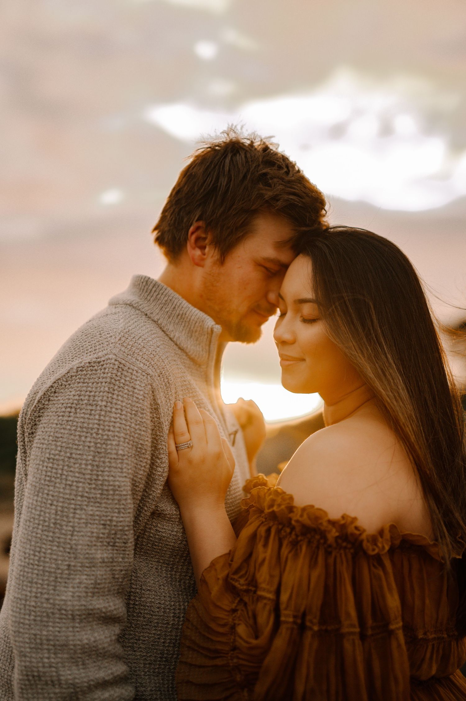 Intimate sunset portrait of couple embracing on beach in warm light.