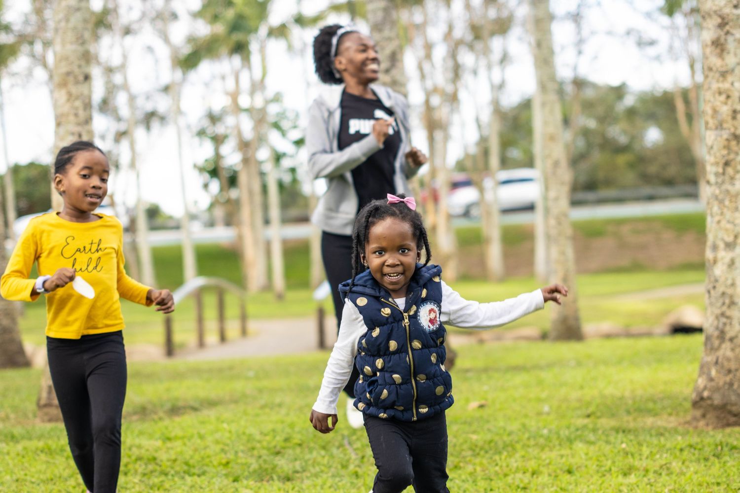 Children playing and running through a park with trees on a sunny day.