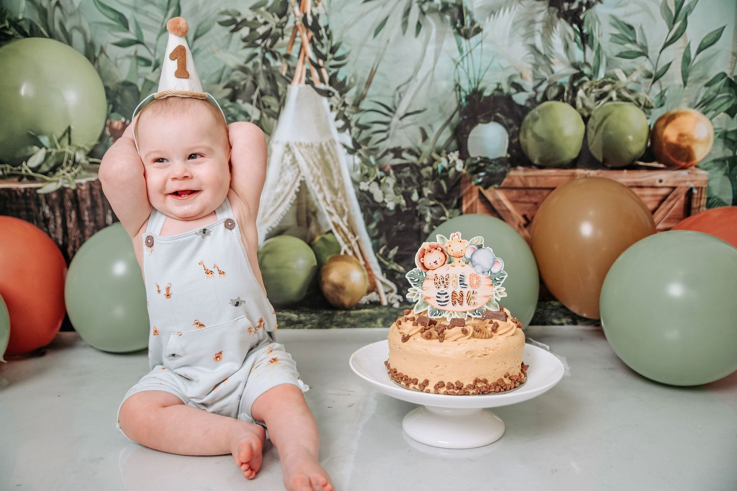 First birthday celebration setup with cake, tropical decor, and smiling baby.