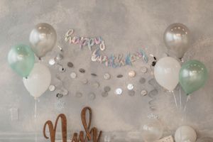 Birthday party decorations with mint and white balloons against a grey wall.