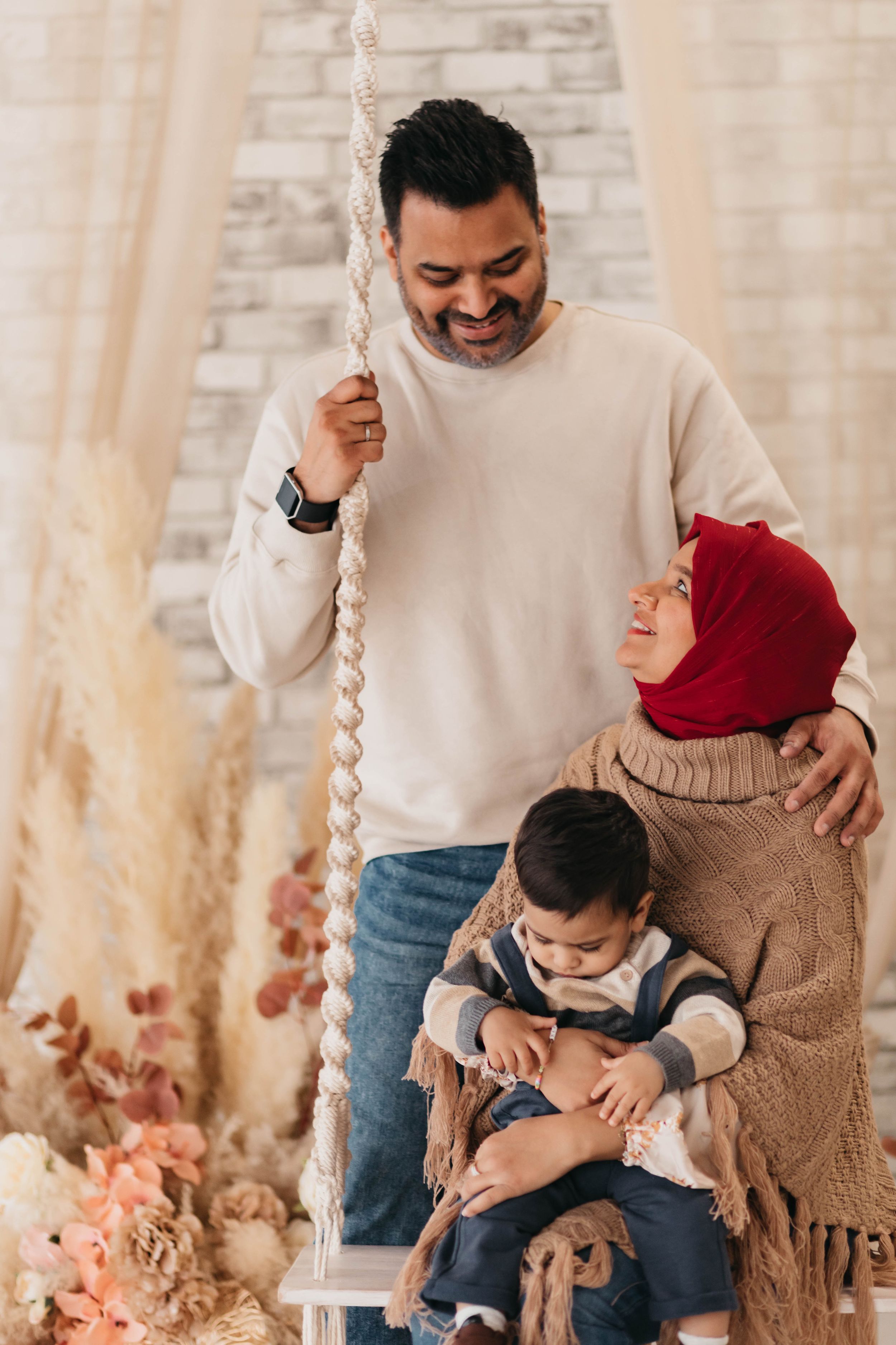 A family shares laughs while posing on a decorative rope swing with dried pampas grass accents.