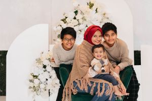 Family portrait with white floral arch backdrop and emerald green seating.
