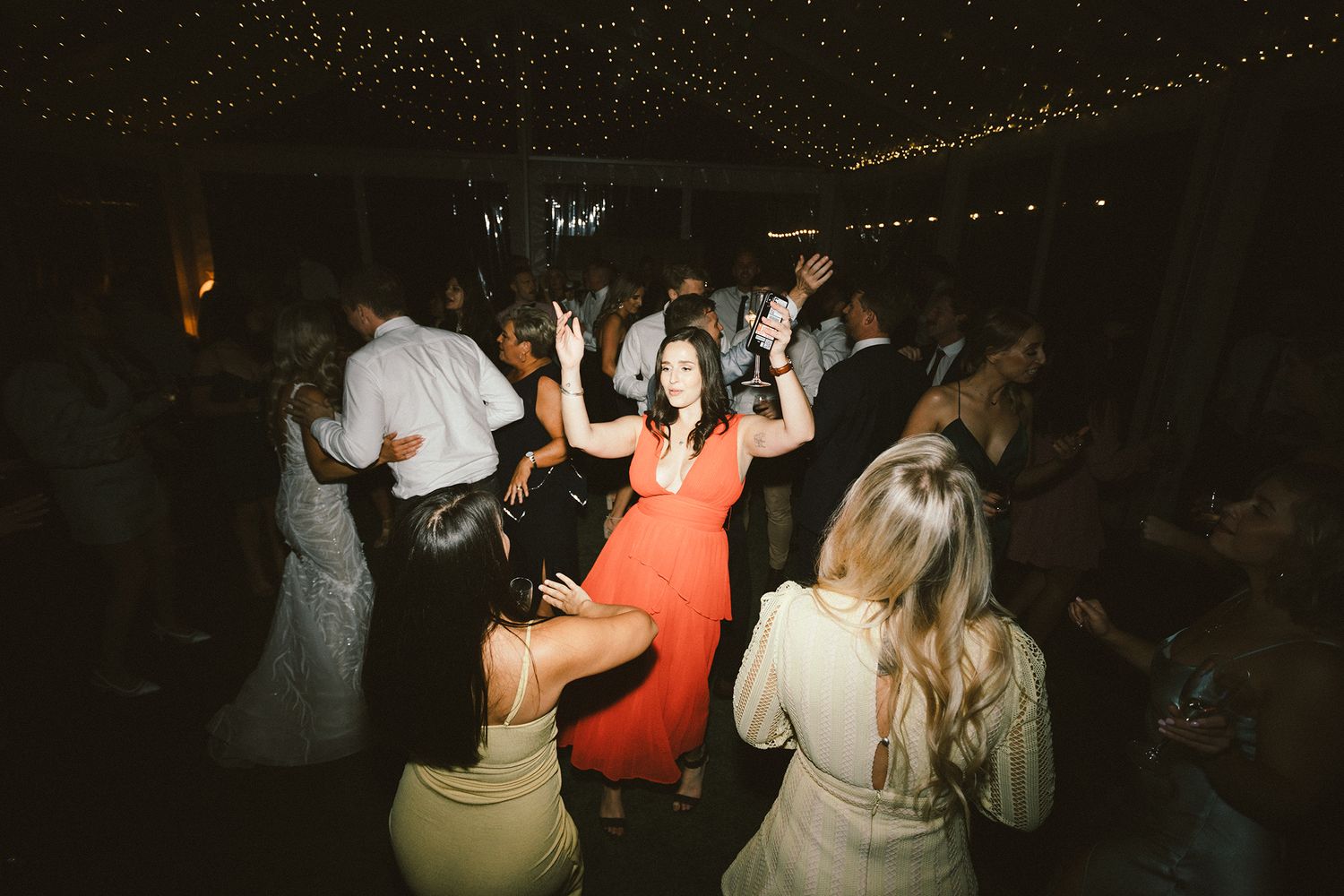 Energetic wedding guests dancing and celebrating under twinkling reception lights.