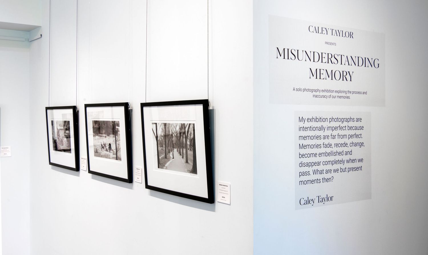 Art gallery wall featuring black and white photographs in frames with exhibition text visible.