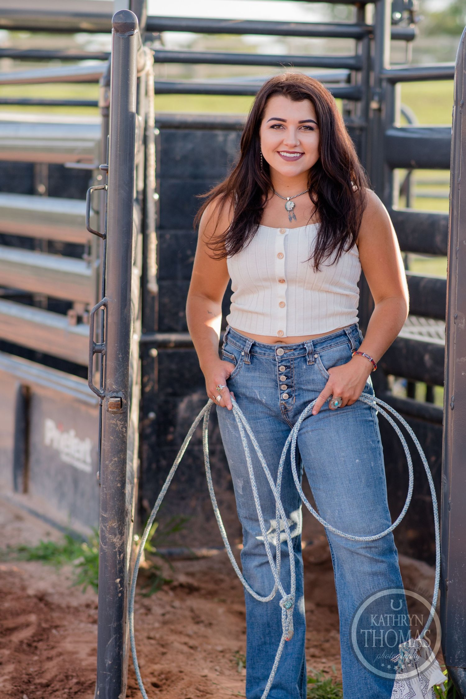 A western photoshoot by a horse corral featuring a casual outfit with jeans and a white crop top.