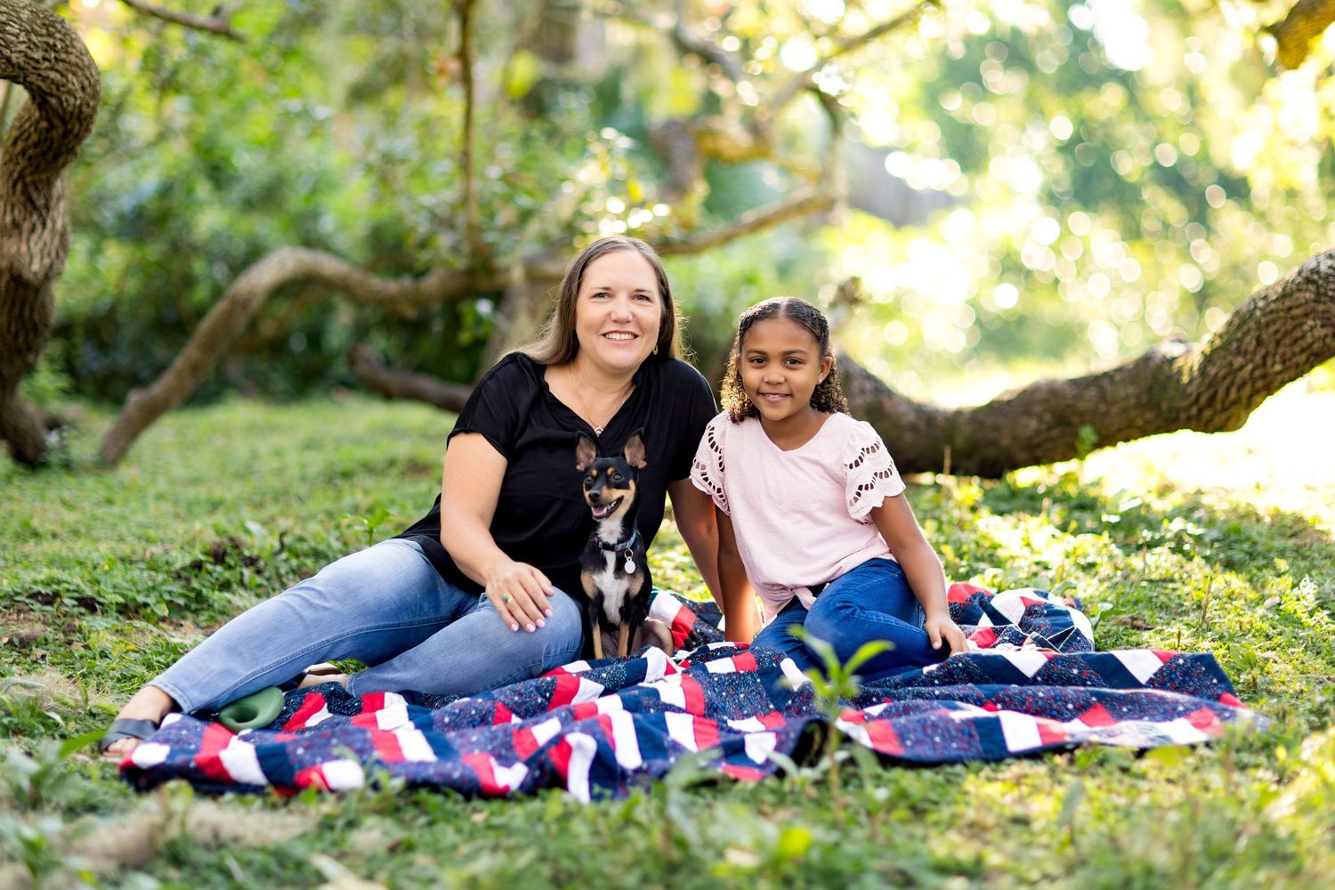 Two people sitting on a colorful blanket in a sunlit garden setting.