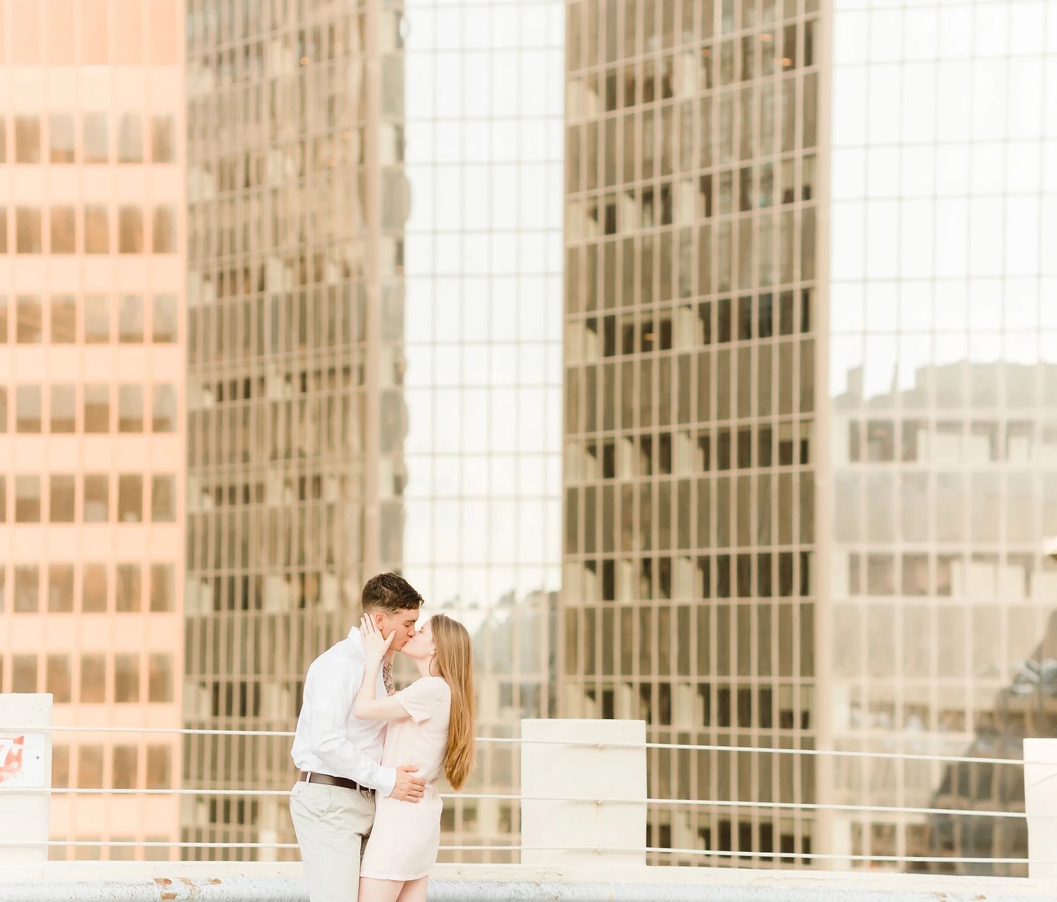 A romantic couple embraces against modern glass buildings at sunset.