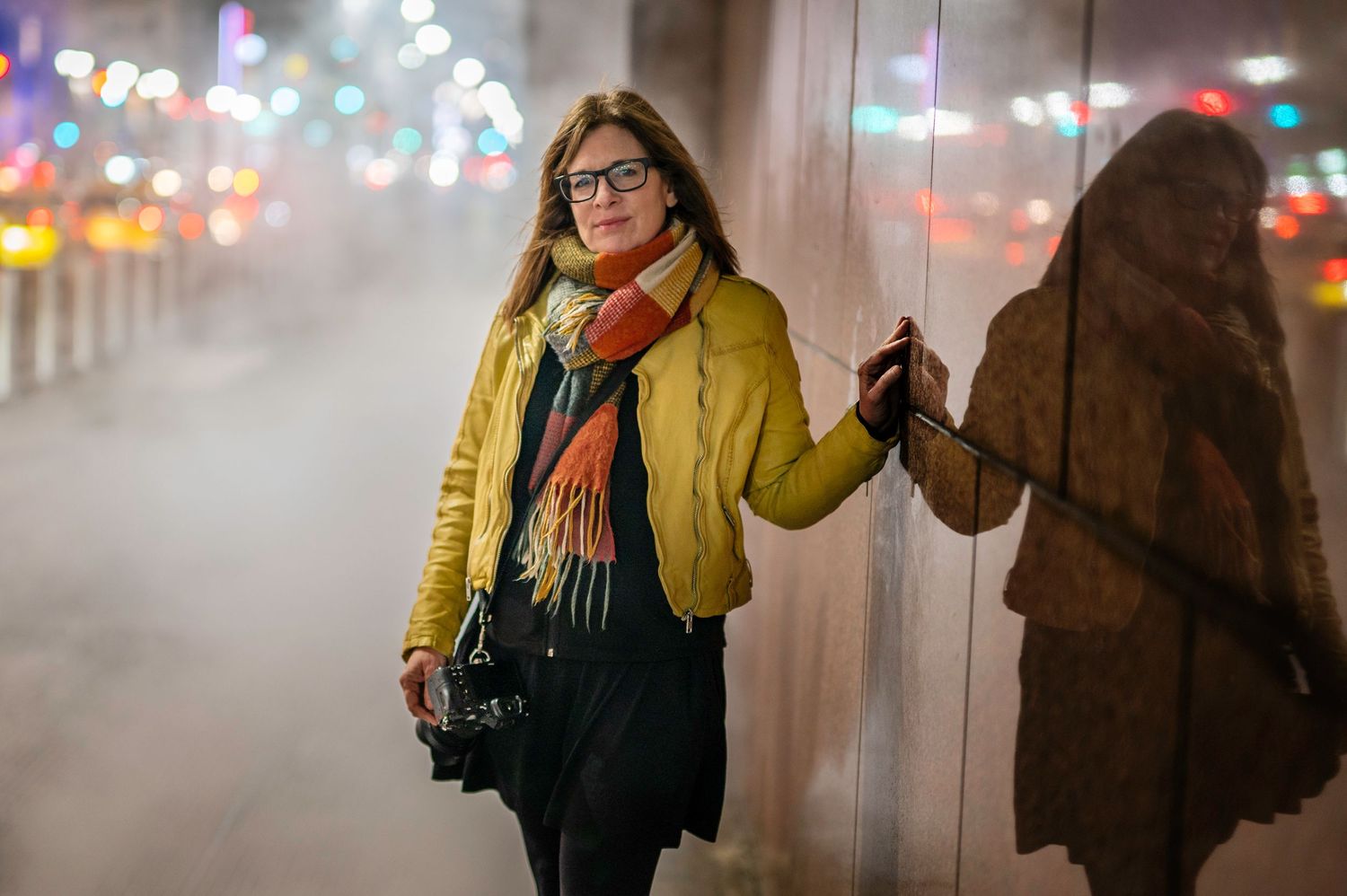 Person in yellow coat and glasses walking along foggy city street at night.