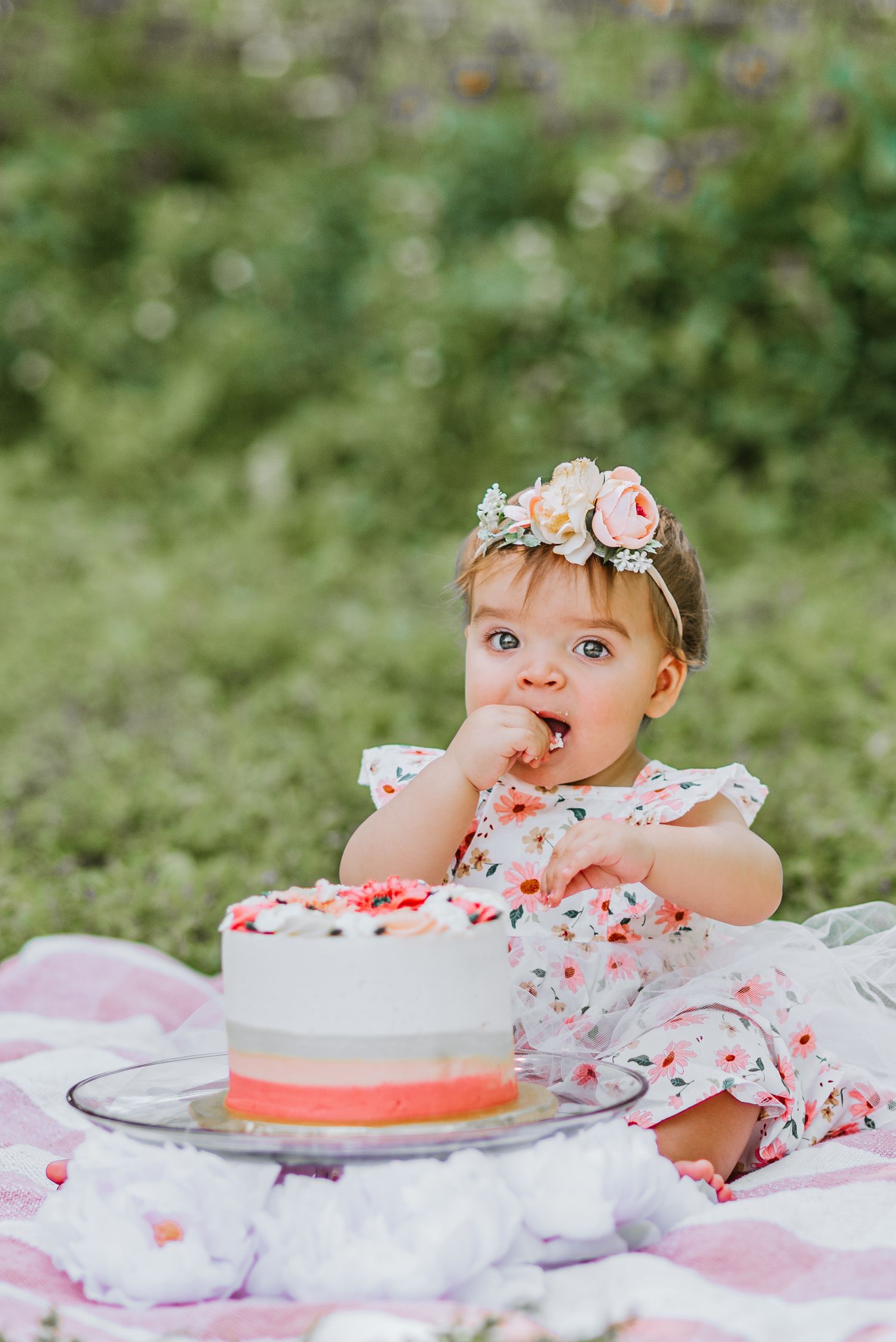 A baby wearing a floral crown has a cake smash photo session with pink frosting and decorations.