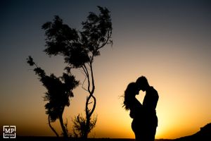 A silhouetted couple embraces against a dramatic sunset sky with a lone tree in the background.