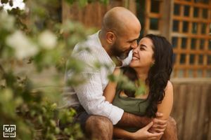 A couple sharing a joyful intimate moment in a garden setting with wooden lattice behind them.