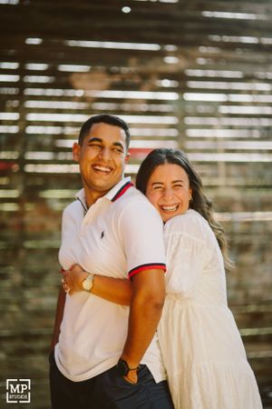 A happy couple smiling and laughing together in front of wooden slat background.