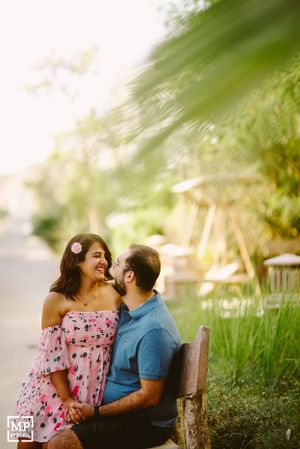 A couple shares a tender moment while sitting on a bench surrounded by lush greenery.