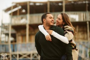 A couple embraces and laughs together in front of a wooden deck structure.