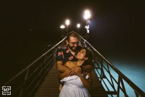 A romantic nighttime embrace on an illuminated pier over dark waters.