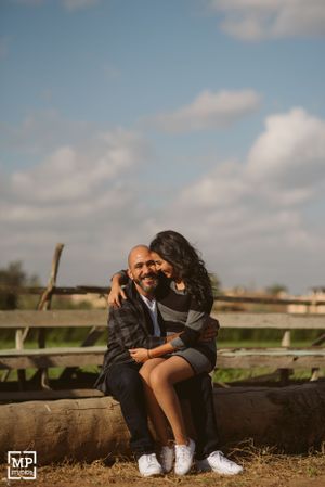 A couple shares a tender moment while sitting on rustic wooden beams under a cloudy sky.