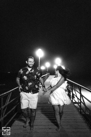 A couple walks together at night on illuminated stairs, with one wearing a floral shirt and shorts.