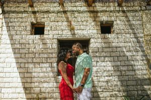 Couple embracing against white stone wall wearing red and green casual outfits.