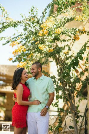 A couple in red and mint outfits embraces under flowering yellow branches.
