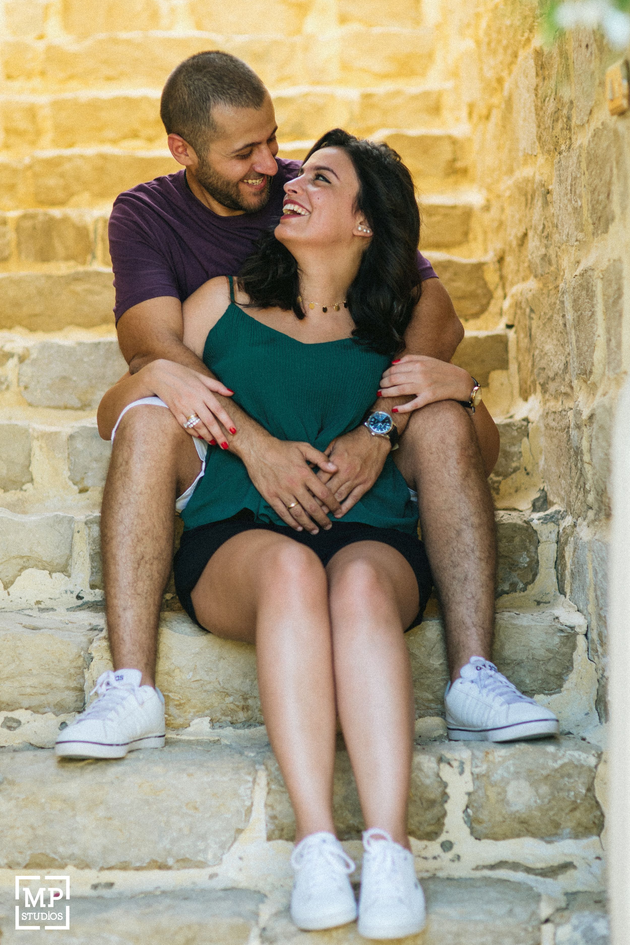 Couple sharing laughter while sitting on stone steps in casual summer attire.