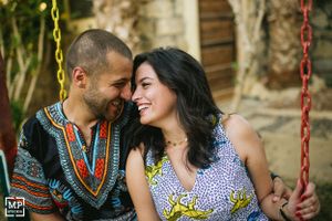 A couple in patterned outfits shares a laugh while sitting on swings.