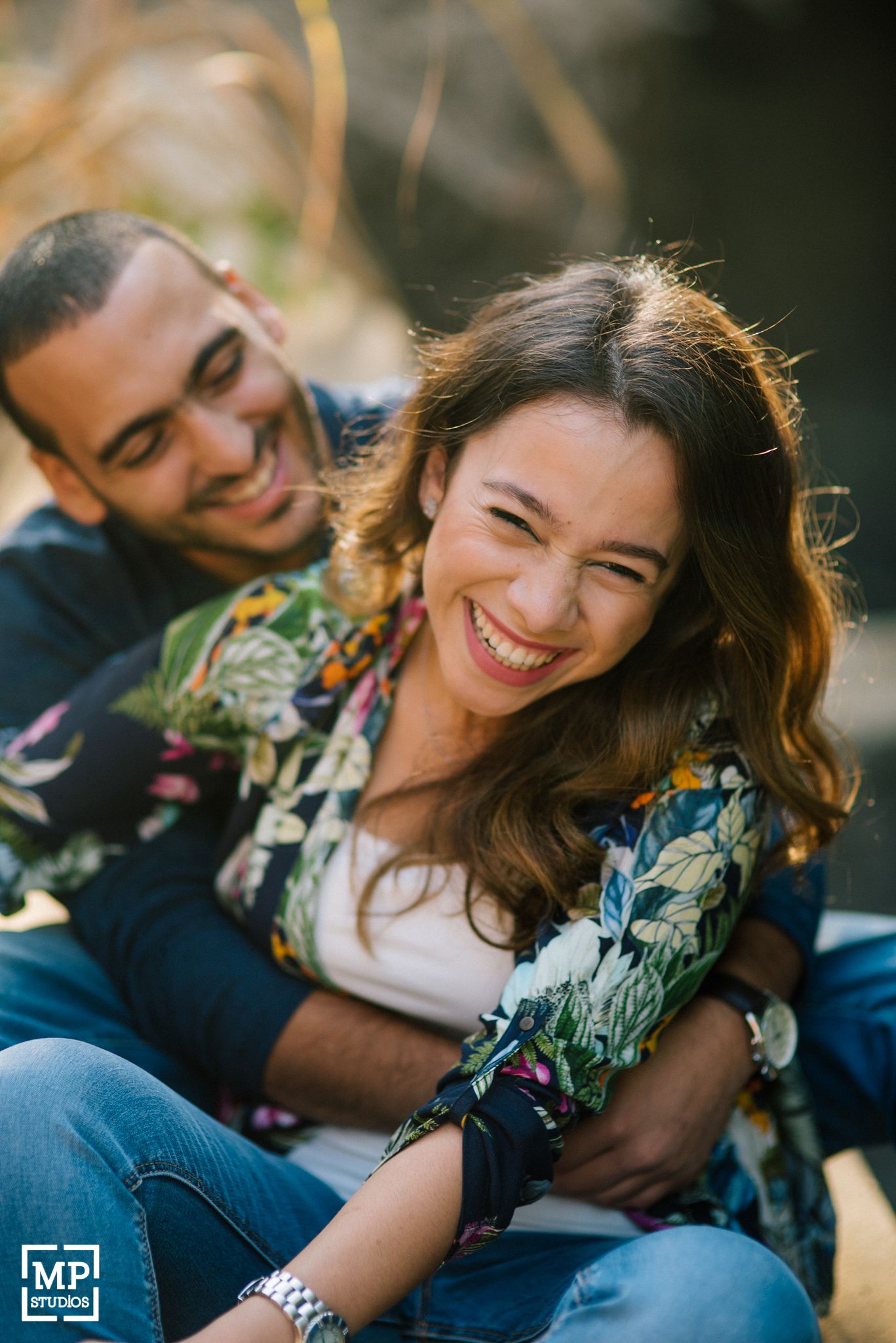 Candid moment of couple laughing in sunlight wearing floral print and casual attire.