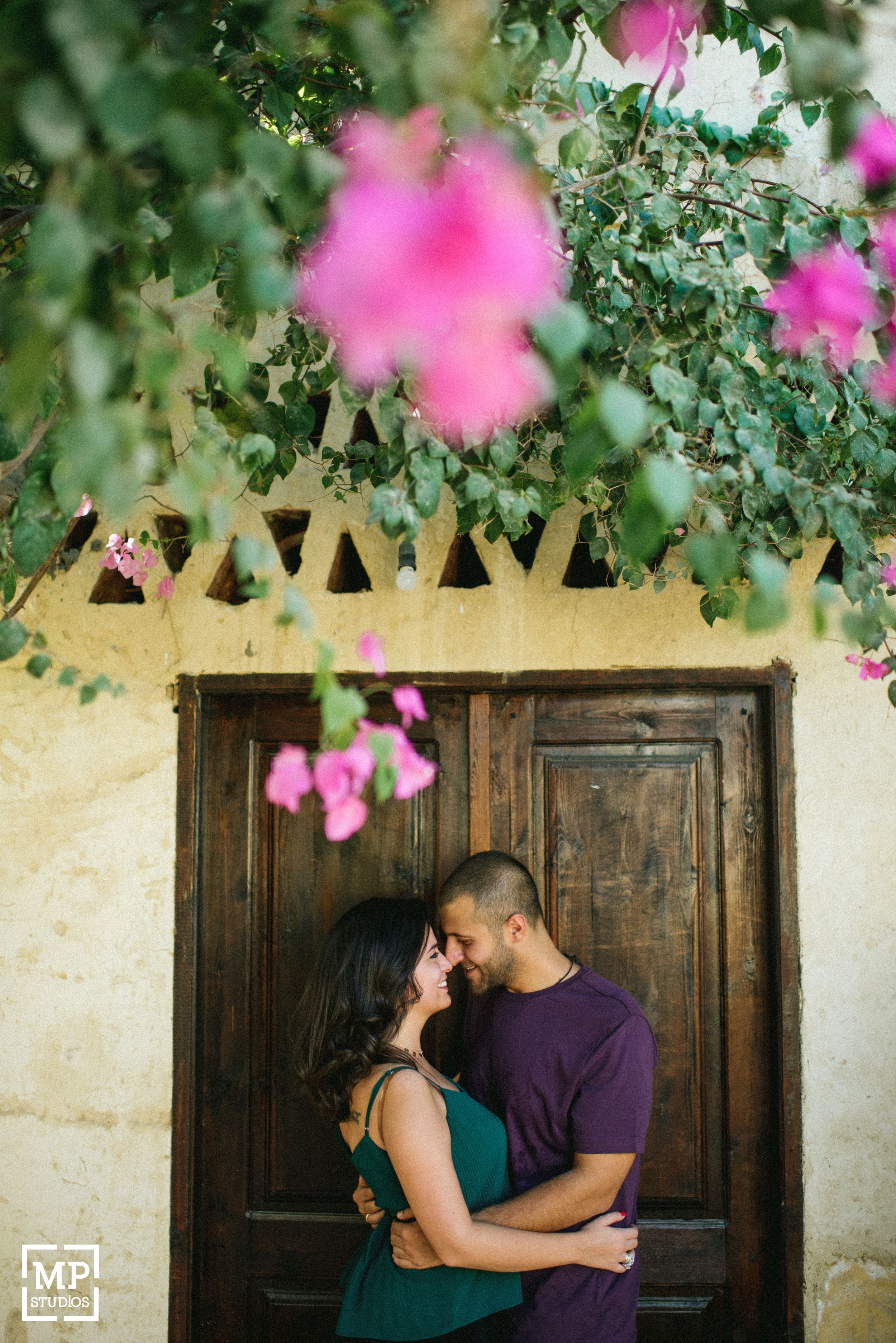 Romantic moment between couple framed by wooden door and pink flowers.