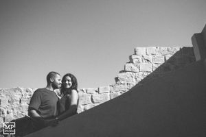 A couple shares a tender moment against a white stone wall in black and white photography.
