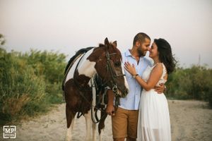 A couple poses with their brown and white horse on a dirt path during a photoshoot.