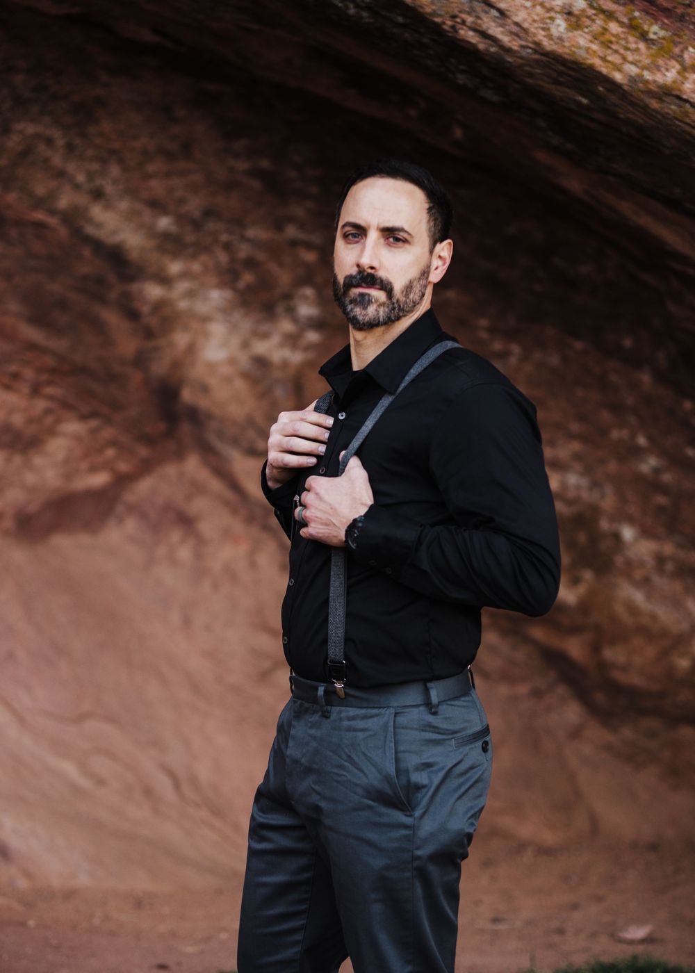 Person in dark formal attire with suspenders poses against red canyon walls.