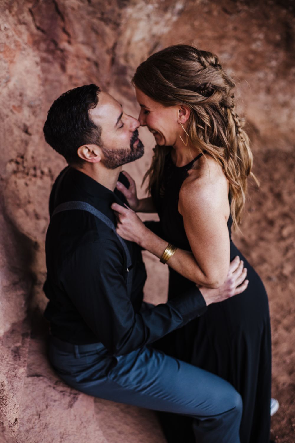 Romantic couple sharing intimate moments against textured red rock wall in dramatic lighting.