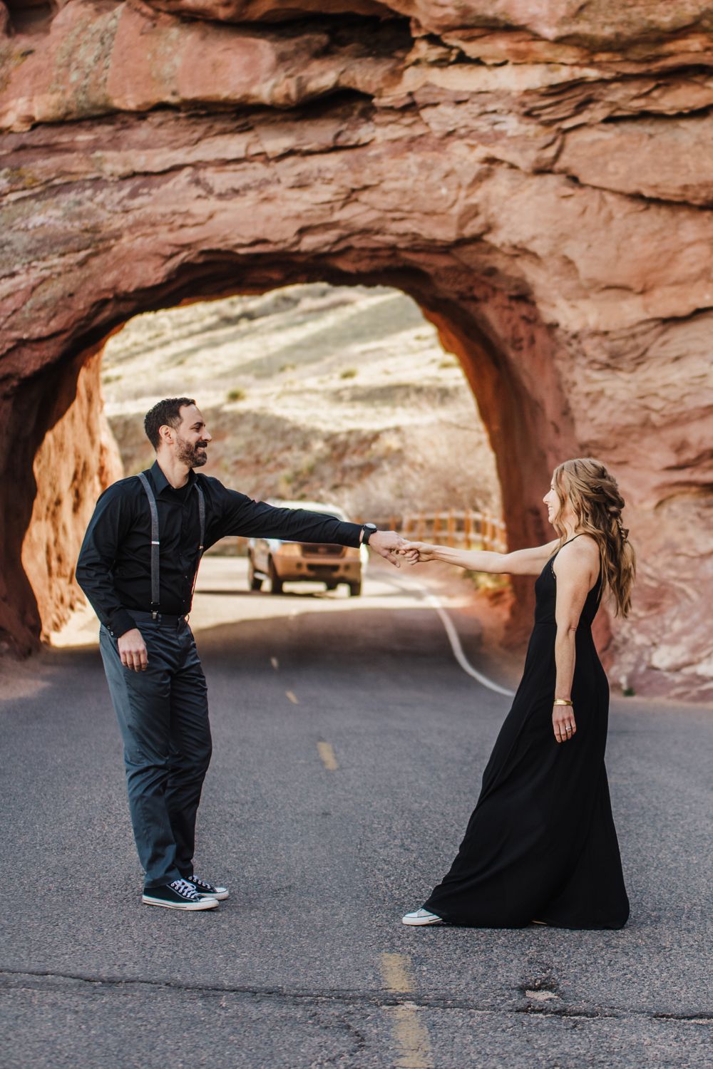 Couple performs playful dance moves under dramatic desert rock arch.