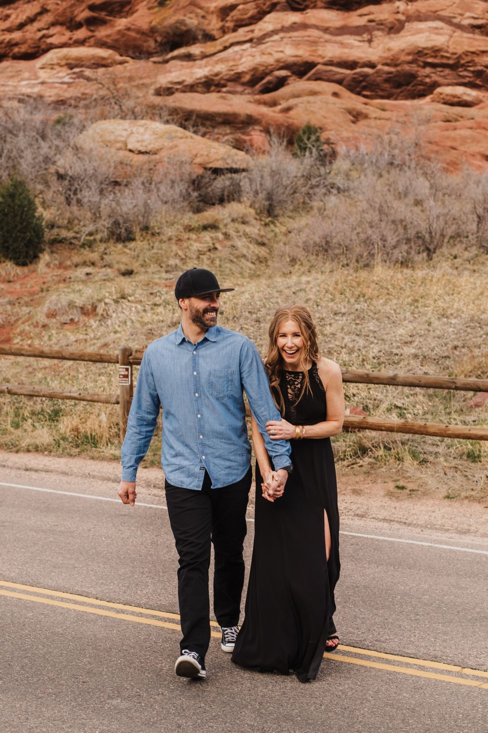 Couple strolls together on paved road with scenic red rock formations in background.