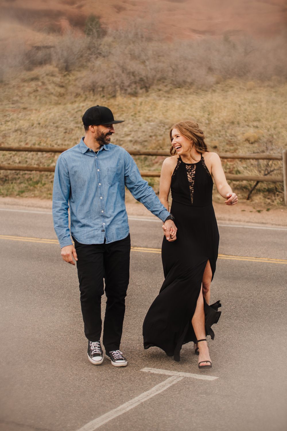 Couple shares playful moment on desert road with red rock cliffs behind them.