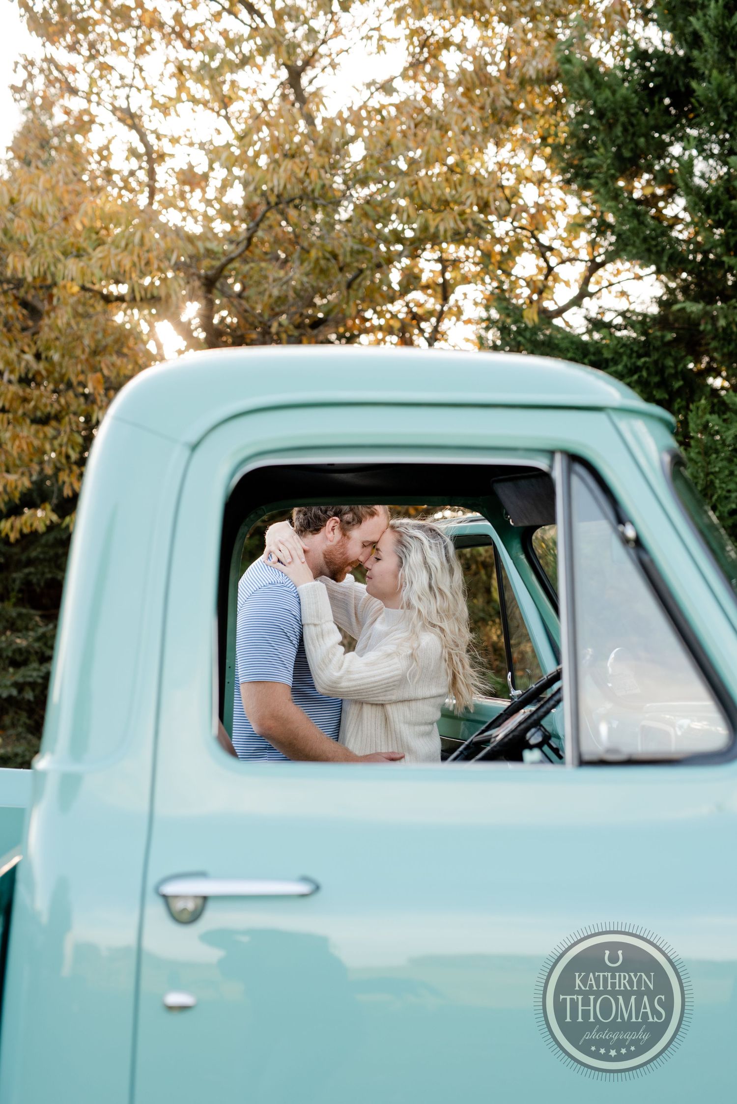 Couple embracing in the cab of a classic mint green pickup truck during golden hour.