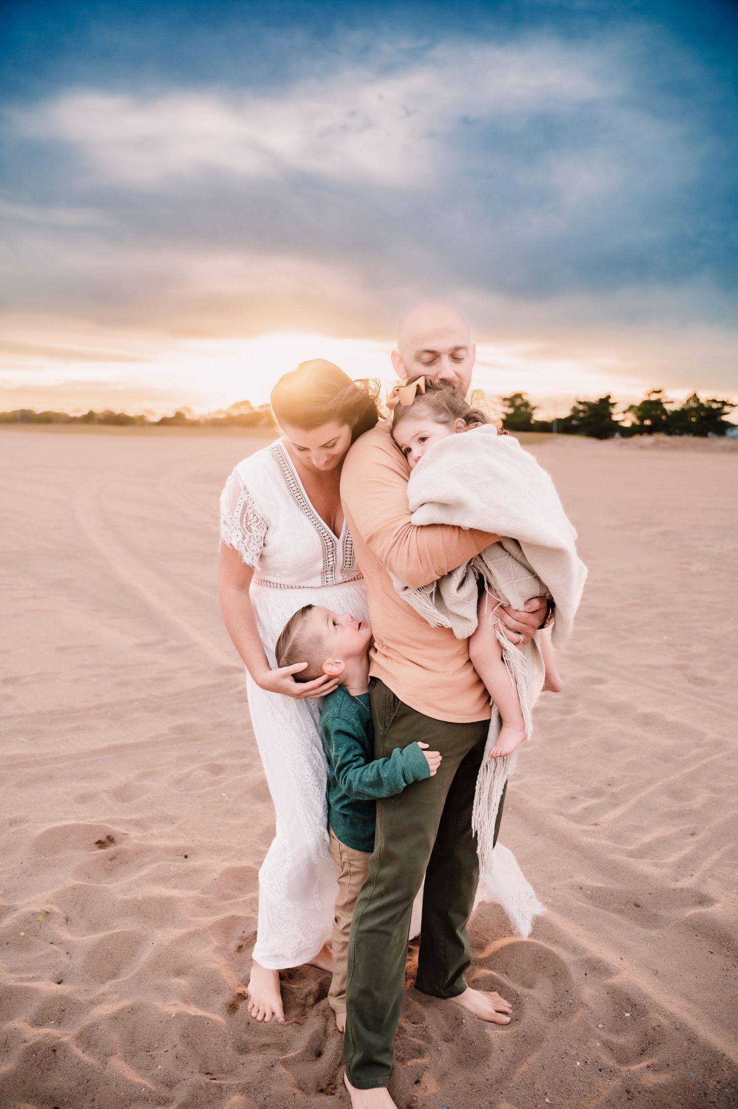 parents standing on south beach in Staten Island NY with dad holding young daughter and mom cuddling sons head
