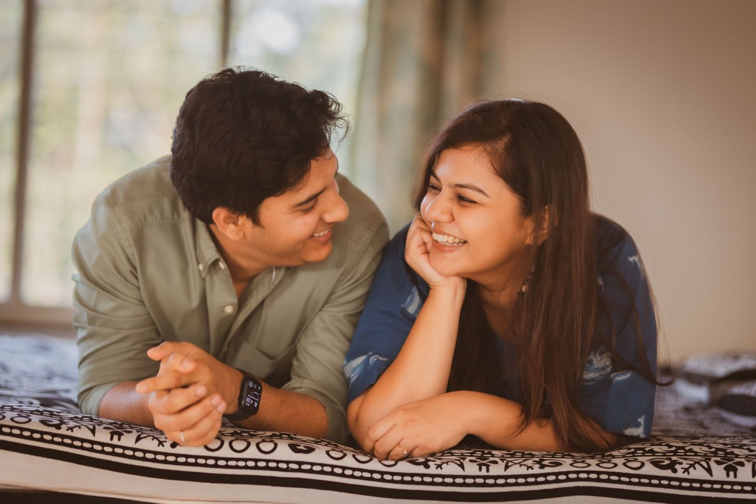 Couple lying on patterned blanket sharing intimate moment indoors.