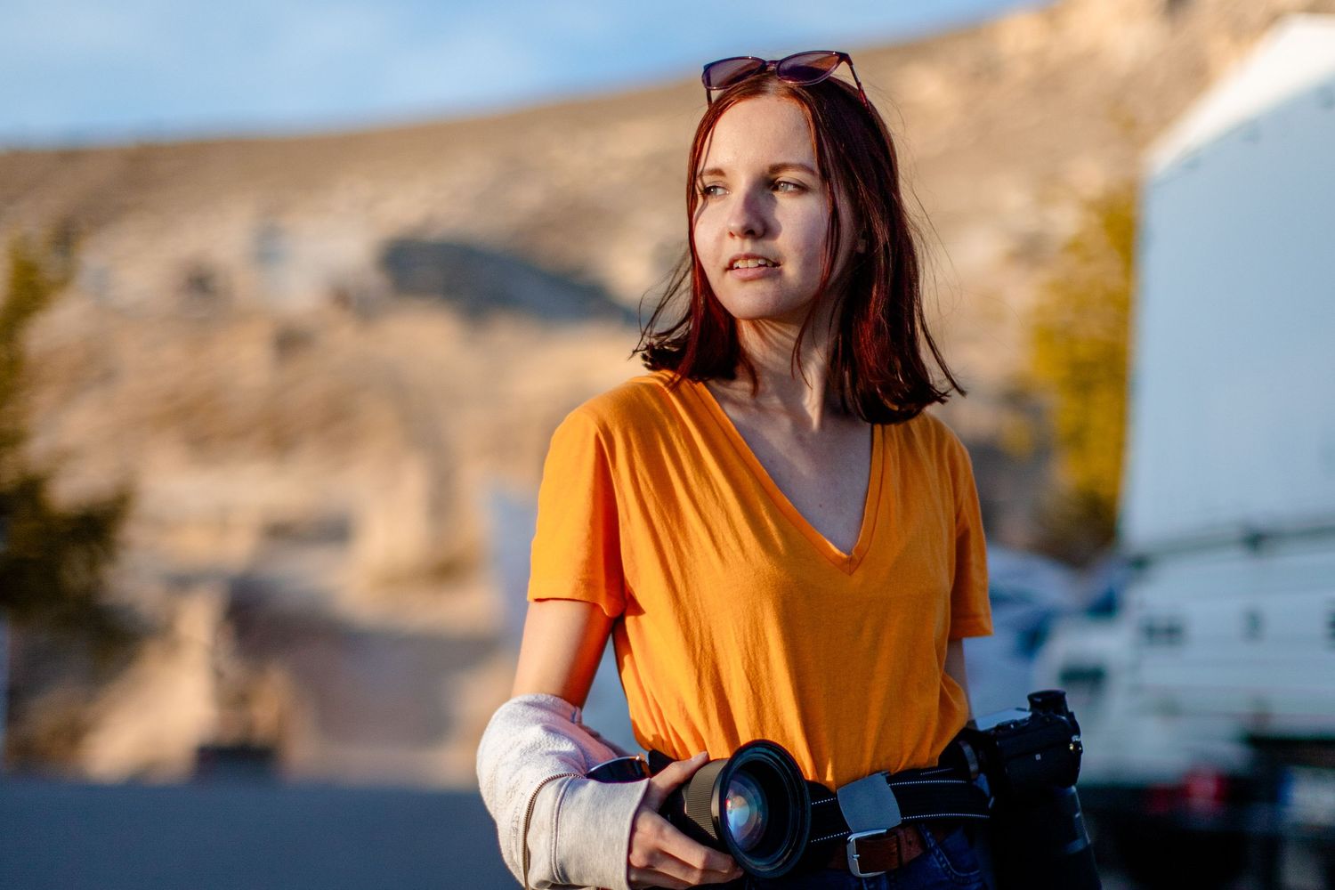 Professional photographer in orange shirt works with camera equipment outdoors.
