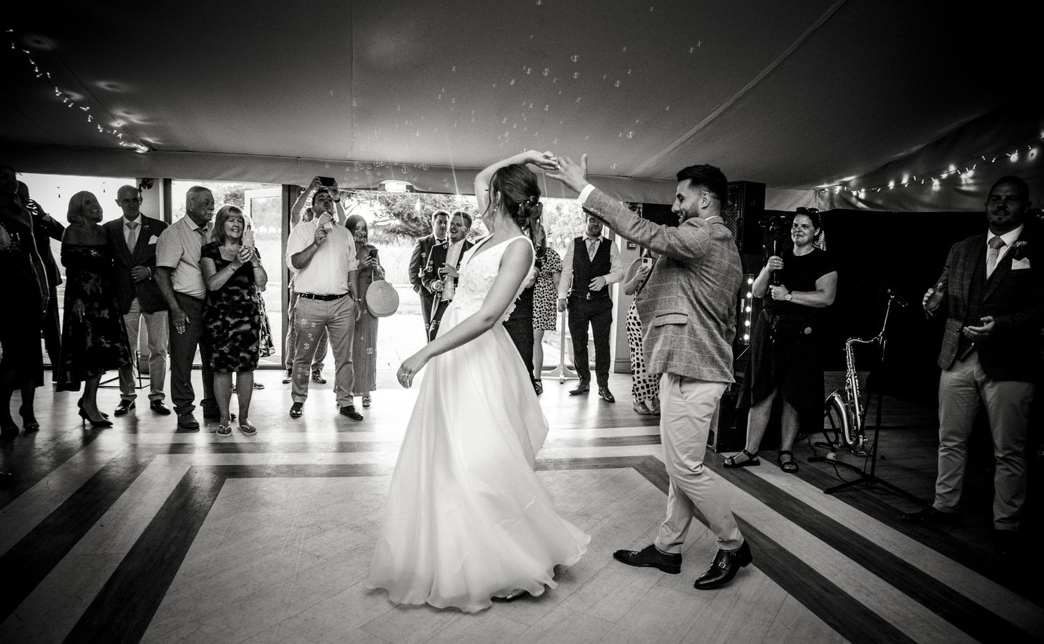 Wedding guests dance and celebrate on a black and white checkered dance floor.