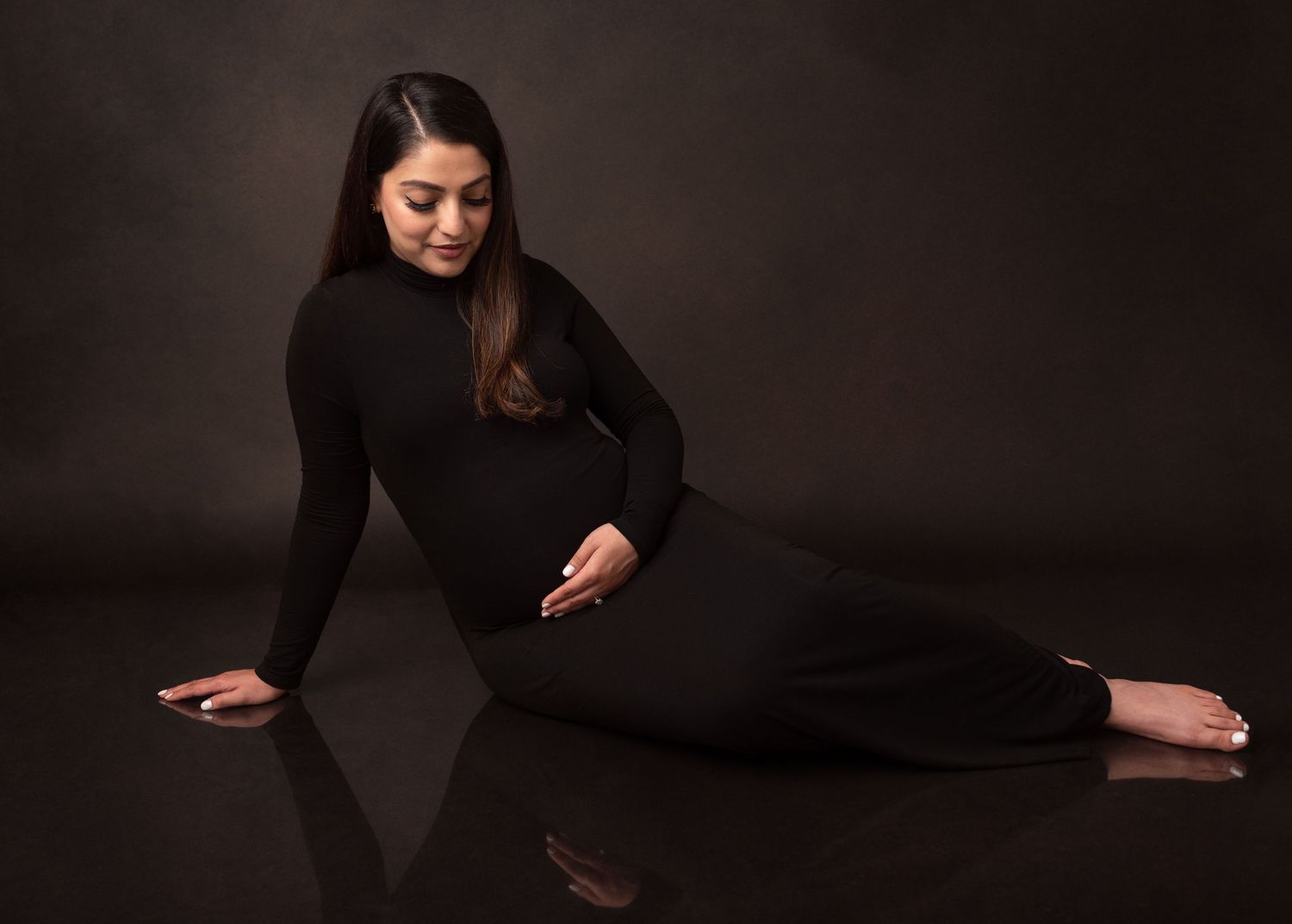 Artistic maternity photo with woman in black dress posing against dark background.