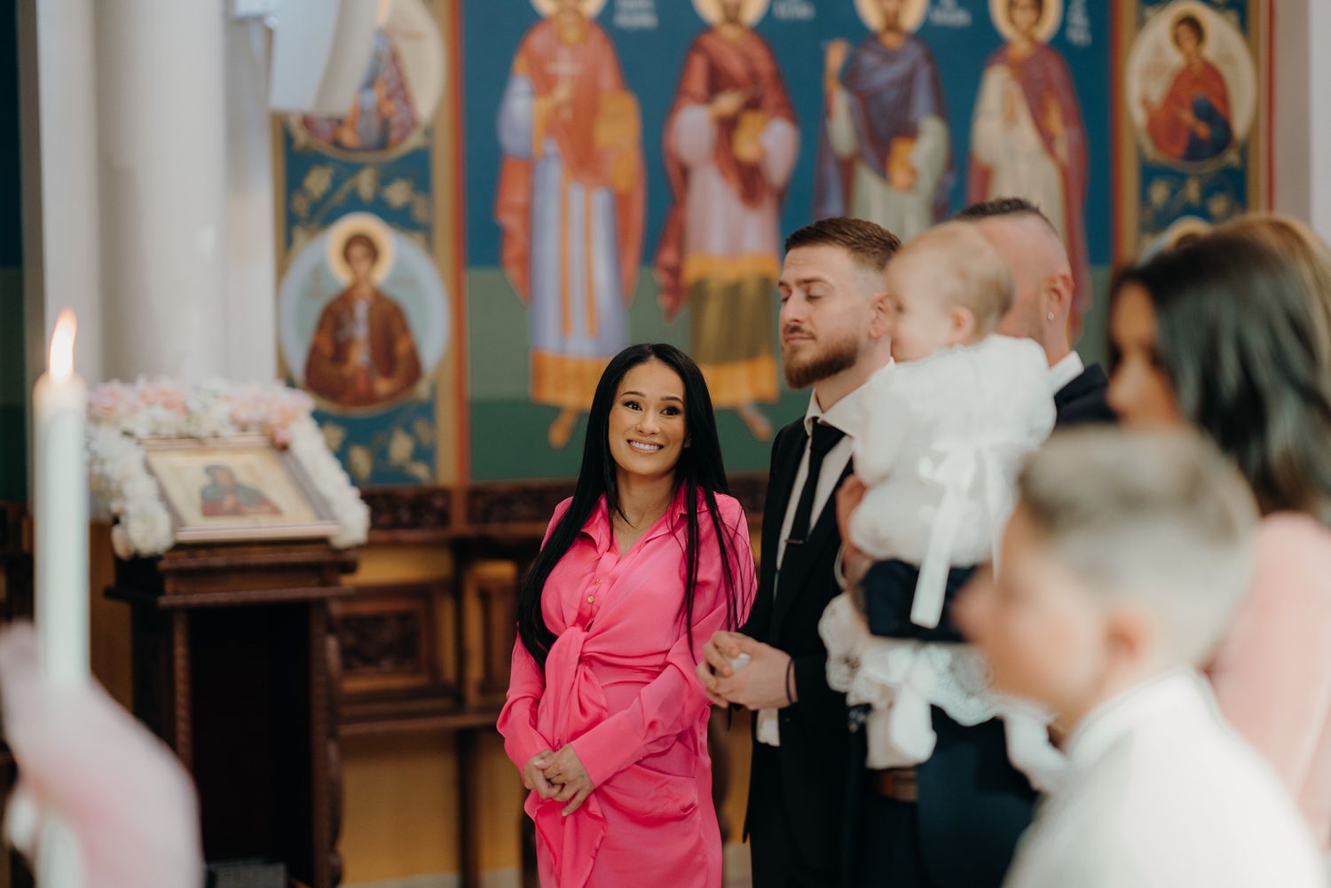 mum in pink dress smiles at daughter who is about to be baptised in the church
