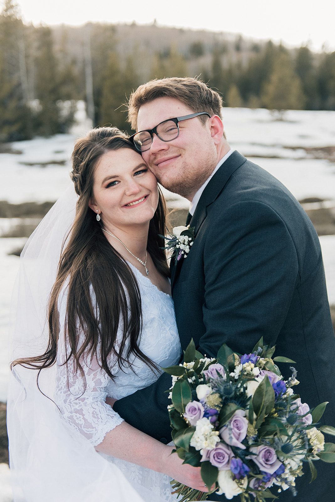 A close-up portrait of a couple on their wedding day with a bouquet of purple and white flowers.