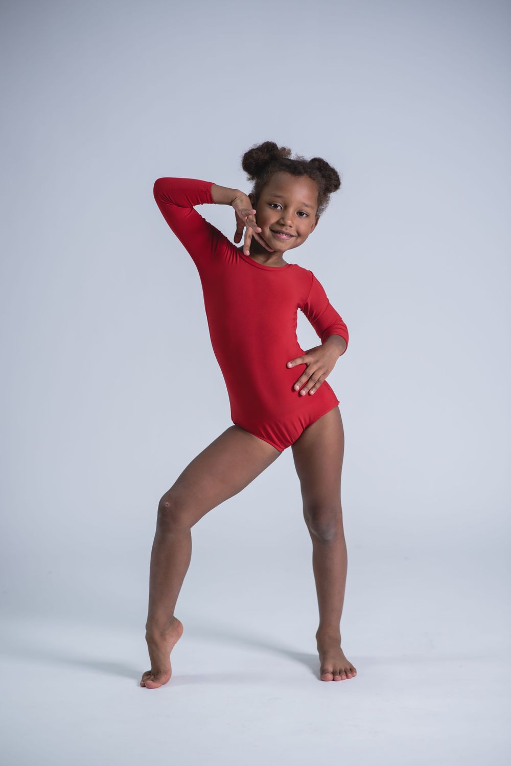 Dancer in red leotard strikes playful pose during dance studio photoshoot.