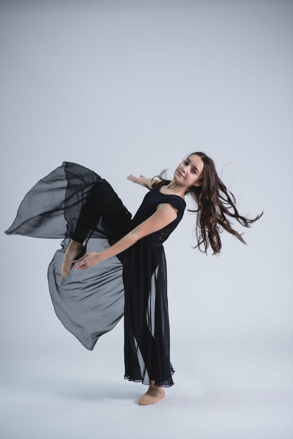 Contemporary dancer in flowing black dress creates dramatic movement with fabric in studio.
