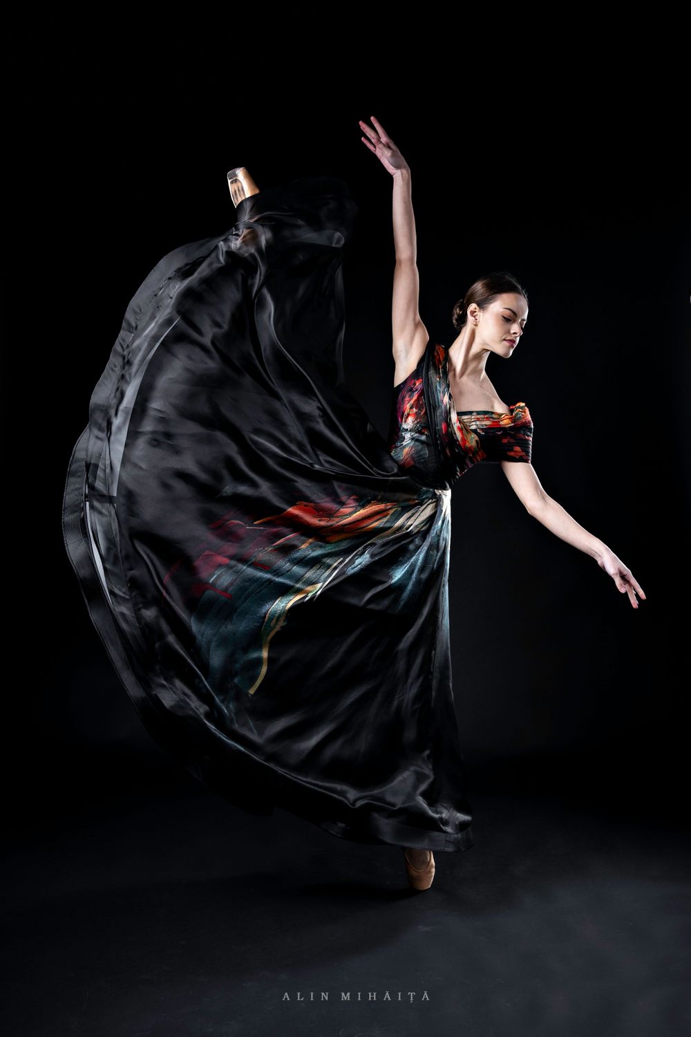 Dancer in flowing black dress creates dramatic movement against dark background.